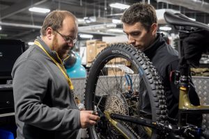 Mechanics at a GO Outdoors store looking at the rear wheel and rear derailleur of a long travel MTB which is in a bike stand.