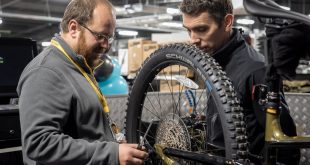 Mechanics at a GO Outdoors store looking at the rear wheel and rear derailleur of a long travel MTB which is in a bike stand.