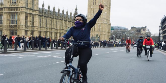 Woman riding bike past the Houses of Parliament